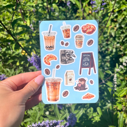 A6 formaat stickervel met allemaal koffie-achtige illustraties. Denk aan iced lattes, een koffiemachine, een otter met koffie, zoete broodjes, koffiebonen, etc.
