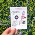 Stickervel A6 met handgetekende illustraties van retro producten zoals oortjes, roze klaptelefoon, een plaat, camera en MP3.