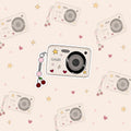 Sticker van een camera in retro look met een hanger eraan van een kers. De camera is versierd met sterretjes en hartjes.