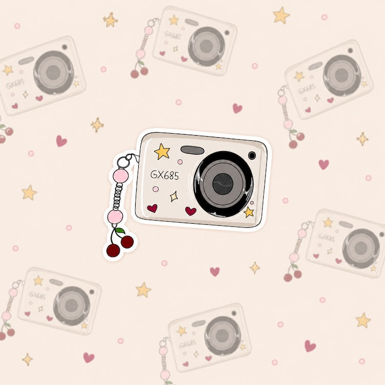 Sticker van een camera in retro look met een hanger eraan van een kers. De camera is versierd met sterretjes en hartjes.